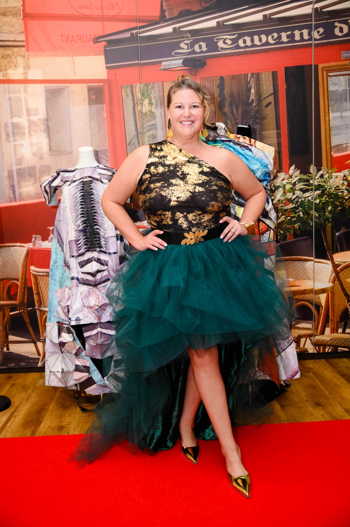 Kristi Straw in a black-and-gold top and green tulle skirt, standing beside wearable art